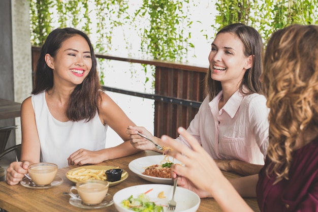 Grupo de três melhores amigos conversando enquanto almoçam juntos em um café