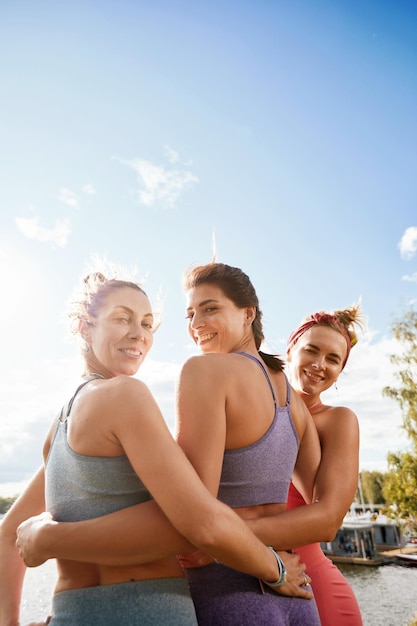 Foto grupo de três mulher aquece no parque antes de correr. conceito de estilo de vida saudável. amigos de mulheres esportivas se divertindo e fazendo diferentes exercícios de alongamento no parque de verão.