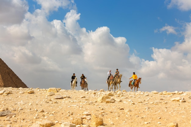 Grupo de turistas montando camelos e cavalos no deserto perto da pirâmide no egito