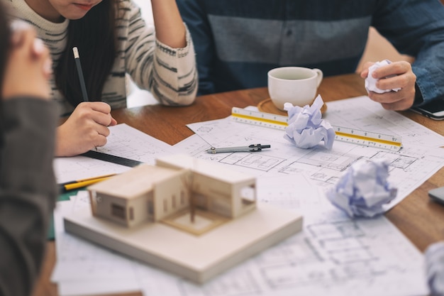 Foto grupo de um arquiteto se sente estressado depois de trabalhar no modelo de arquitetura, juntamente com o papel de desenho de loja na mesa no escritório