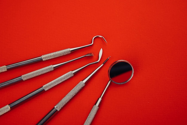 Grupo de utensílios odontológicos para o tratamento dos dentes em close-up de fundo vermelho.