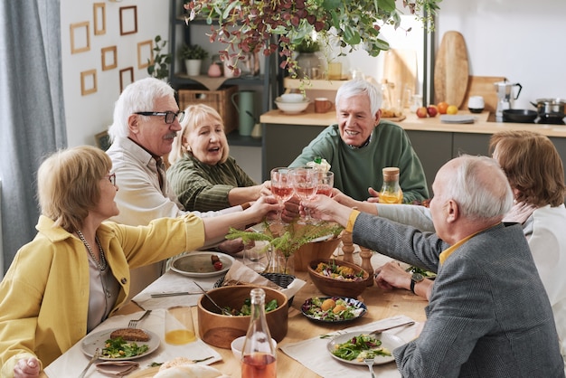 Grupo de velhos amigos brindando com taças de vinho tinto enquanto está sentado à mesa durante o jantar em casa
