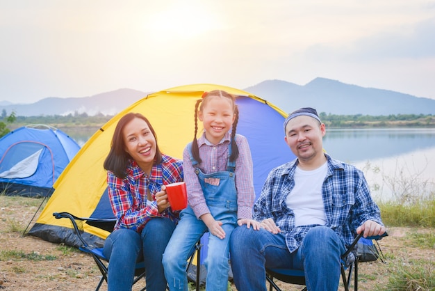 Grupo de viagem em família e acampamento à beira do lago na floresta sentados todos juntos e sorrindo