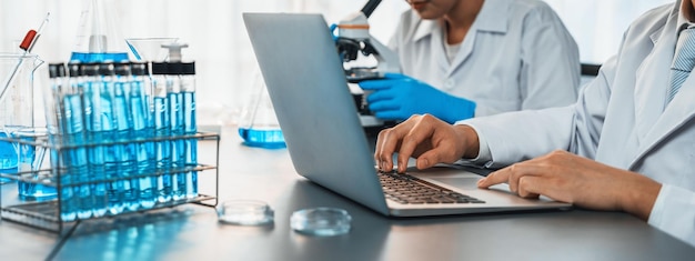 Un grupo dedicado de científicos realiza experimentos químicos e investigaciones en laboratorios médicos como desarrollo innovador para una nueva vacuna o antibiótico y estudia los resultados de las pruebas en una computadora portátil Neoteric