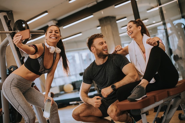 Grupo de deportistas en ropa deportiva tomando fotos selfie con teléfono móvil en el gimnasio