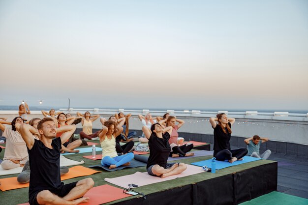 Grupo de diferentes personas están haciendo prácticas de yoga meditativo en la azotea en una hermosa puesta de sol en las noches de verano