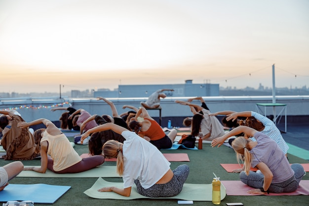 Grupo de diferentes personas están haciendo prácticas de yoga meditativo en la azotea en una hermosa puesta de sol en las noches de verano