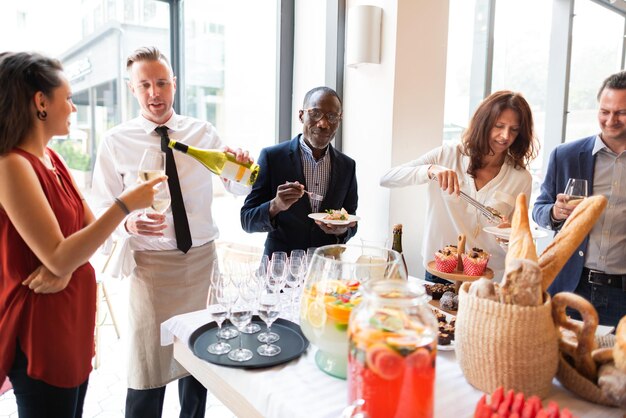 Grupo disfrutando de una reunión casual con bebidas y comida Diversa mezcla de personas socializando compartiendo vino y bocadillos en un entorno moderno brillante Diversas personas se mezclan en un evento social en un restaurante