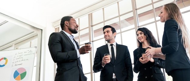 Grupo de diversidad de empresarios estrictamente vestidos con trajes reunidos junto a la ventana de la oficina Trabajadores administrativos africanos y caucásicos teniendo conversaciones y discusiones informales