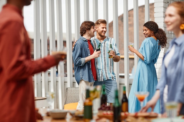 Grupo diversificado de amigos curtindo festa ao ar livre no terraço iluminado pela luz do sol