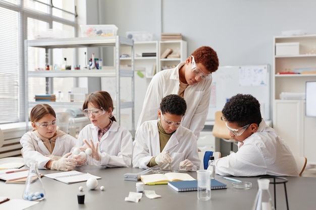 Grupo diversificado de crianças vestindo jalecos desfrutando de experimentos na aula de química no espaço de cópia da escola