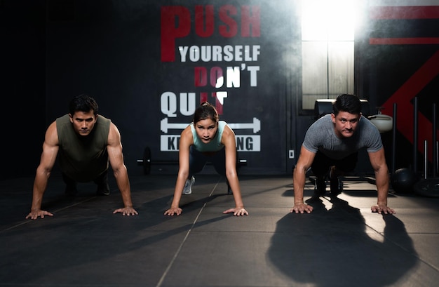 Grupo diversificado de homens e mulheres em forma em flexões de exercícios de roupas esportivas no chão na academia de ginástica