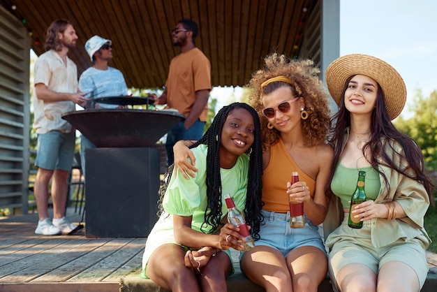 Grupo diversificado de meninas olhando para a câmera enquanto desfruta de festa ao ar livre com amigos na cabana de verão