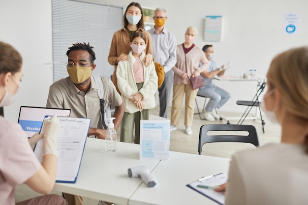 Grupo diversificado de pessoas esperando na fila para se registrar para a vacina contra a vacina no centro de vacinação, copie o espaço