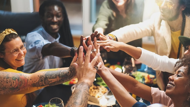 Grupo diversificado de pessoas sentando-se à mesa de jantar de mãos dadas - Grupo multiétnico de amigos se divertindo cooperando - conceito de sucesso e força - foco na mão da frente
