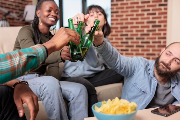 Grupo diversificado de pessoas tilintando garrafas de cerveja em casa, dizendo aplausos e fazendo brindes para comemorar a reunião. Amigos felizes brindando com bebidas alcoólicas, comemorando evento social.