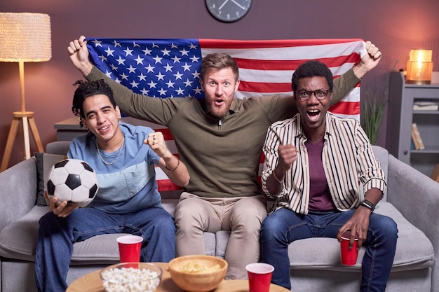 Grupo diverso de aficionados al deporte viendo el partido ondeando la bandera de EE.UU.