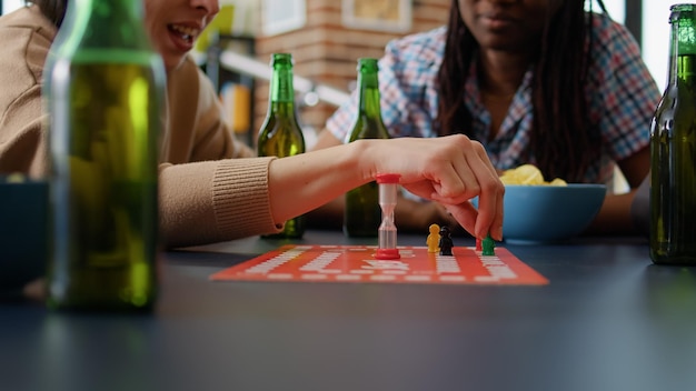 Grupo diverso de amigos jugando juegos de mesa de charadas y reuniones divertidas, disfrutando de actividades de ocio con cartas y figuritas. Gente riéndose y divirtiéndose con un juego competitivo. De cerca.