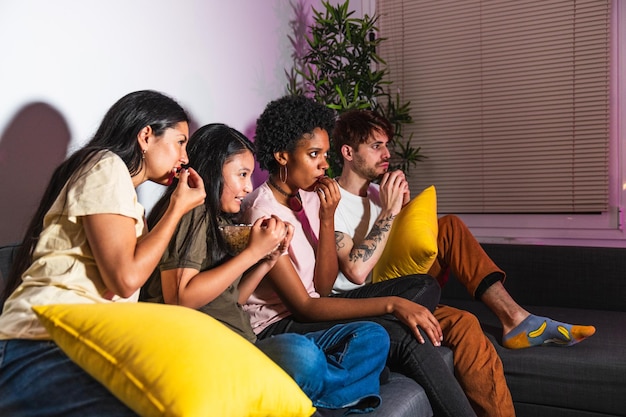 Un grupo diverso de amigos viendo una película de suspenso compartiendo palomitas de maíz en una noche acogedora