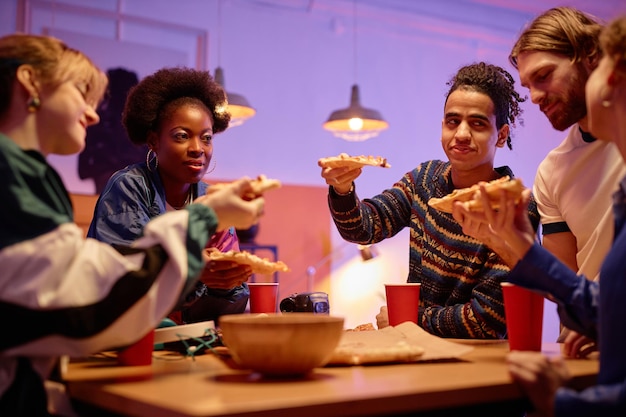 Grupo diverso de jóvenes comiendo pizza en la fiesta de la casa