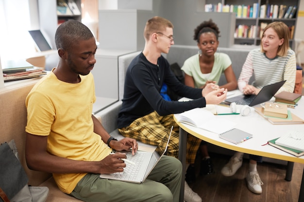 Grupo diverso de jóvenes que estudian juntos en la mesa en la biblioteca de la universidad se centran en africanamerican ...