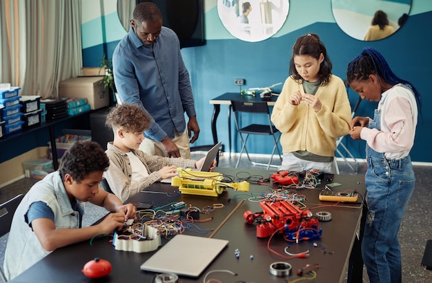 Grupo diverso de niños adolescentes construyendo robots juntos mientras disfrutan de la clase de ingeniería en moder