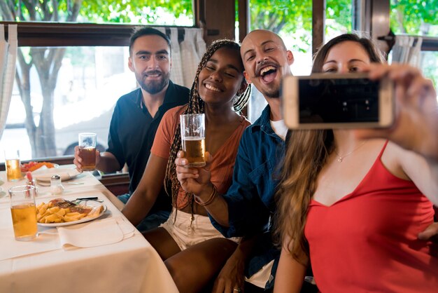 Grupo de diversos amigos tomando un selfie con un teléfono móvil mientras disfrutan de una comida juntos en un restaurante. Concepto de amigos.