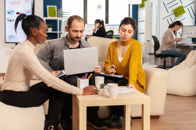 Grupo de diversos colegas emprendedores de empresas emergentes sentados en el sofá en el lugar de trabajo profesional, brifando y compartiendo ideas sobre la gestión de la estrategia financiera