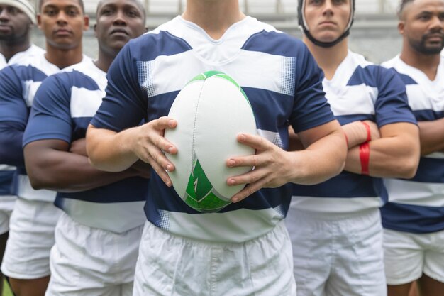 Foto grupo de diversos jugadores de rugby masculinos de pie juntos con una pelota de rugby en el estadio