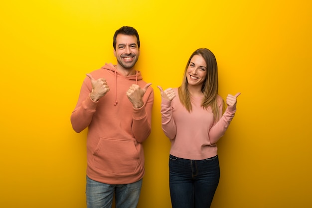 Grupo de dos personas en el fondo amarillo que da un pulgar hacia arriba gesto