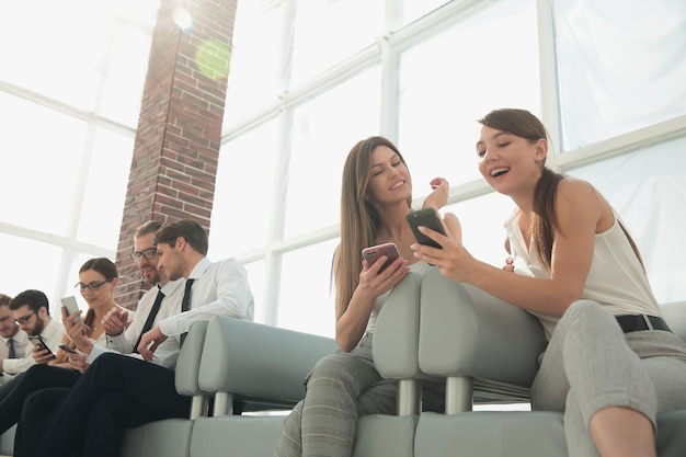 Grupo de empleados con teléfonos móviles sentados en el vestíbulo de la oficina foto con espacio de texto