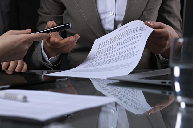 Grupo de empresarios y abogados discutiendo contratos sentados en la mesa. La jefa está tomando un bolígrafo para firmar papeles. Iluminación de bajo perfil.