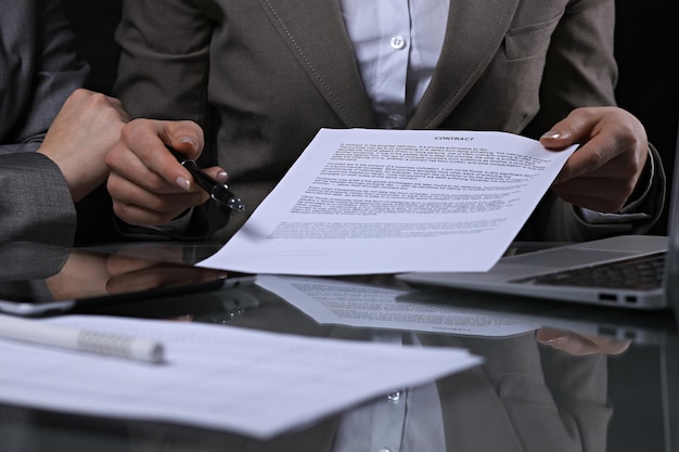 Grupo de empresarios y abogados discutiendo contratos sentados en la mesa. La jefa está tomando un bolígrafo para firmar papeles. Iluminación de bajo perfil.