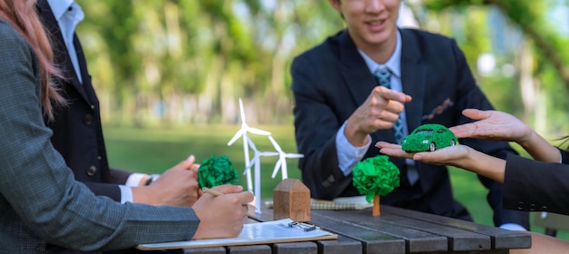 Grupo de empresarios asiáticos presentando un plan de desarrollo respetuoso con el medio ambiente y un proyecto de tecnología sostenible para un futuro más verde estableciendo una oficina de negocios ecológicos al aire libre en el parque natural Gyre