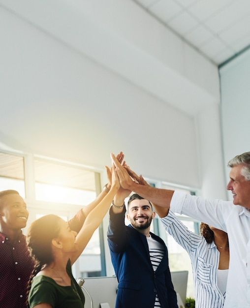 Grupo de empresarios chocando los cinco juntos mientras están de pie dentro de una oficina con bengalas solares y espacio para copiar Equipo de colegas compañeros de trabajo y empleados celebrando el trabajo en equipo y apilando manos