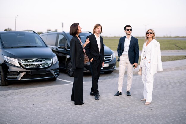 Foto un grupo de empresarios elegantes conversan mientras están juntos en un estacionamiento cerca de vehículos al aire libre colegas y socios comerciales hablando durante un descanso al aire libre al atardecer