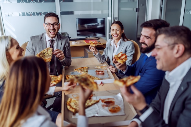 Grupo de empresarios sentados en la sala de juntas, charlando, riendo y comiendo pizza para el almuerzo.