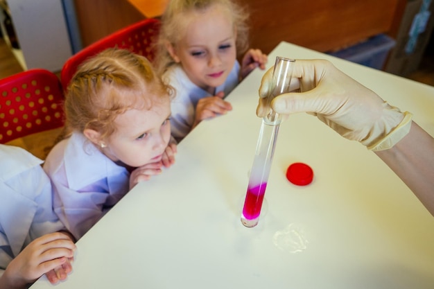 grupo de escolares con maestra en laboratorio escolar haciendo experimentos observando la reacción química con el tinte con vinagre y volcán de soda usando vidrio uniforme de vestido blanco