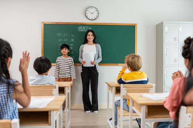 Grupo de estudiantes aprenden con la maestra en el aula de la escuela primaria atractiva hermosa maestra instructora explica y educa a los niños pequeños con felicidad y actividad divertida en el jardín de infantes