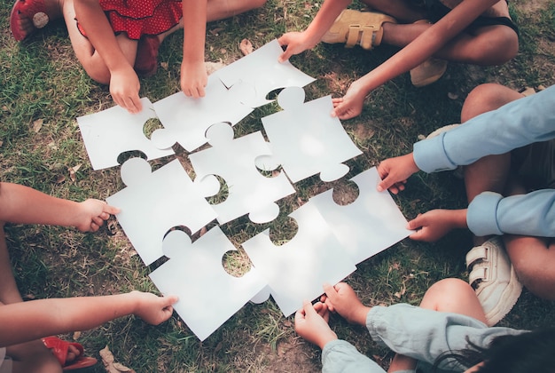 Un grupo de estudiantes étnicamente diversos se unen para jugar rompecabezas / rompecabezas juntos en el patio de recreo. Concepto de trabajo en equipo, cooperación, aprendizaje y educación.