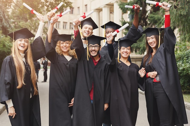 Un grupo de estudiantes graduados multiétnicos celebrando con su diploma. Concepto de educación, cualificación y vestido.