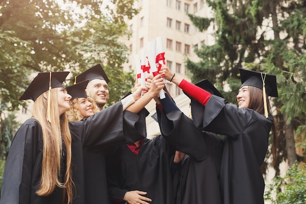 Un grupo de estudiantes graduados multiétnicos celebrando con su diploma. Concepto de educación, cualificación y vestido.