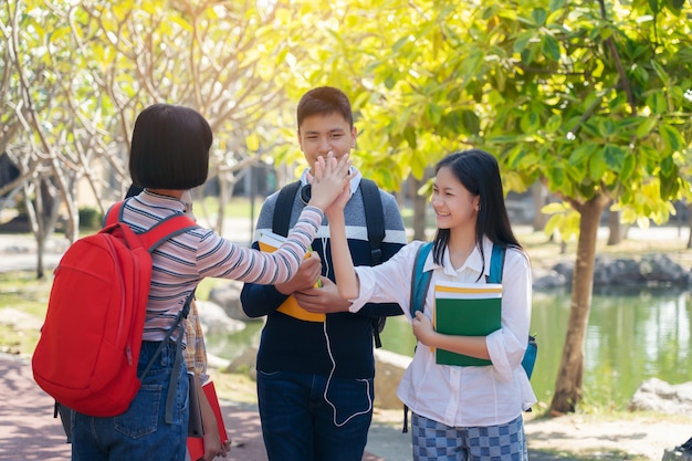 Grupo de estudiantes jóvenes felices tocan las manos al aire libre, concepto de libro de jóvenes estudiantes diversos al aire libre