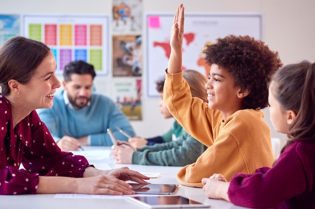 Grupo de estudiantes multiculturales con profesores en el aula levantando la mano para responder a la pregunta