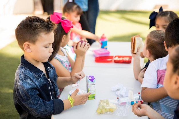 Grupo de estudiantes de preescolar almorzando juntos en un receso escolar al aire libre