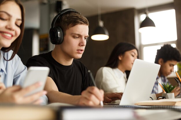 Un grupo de estudiantes que estudian en la biblioteca de la universidad se centran en un tipo serio mirando una computadora portátil