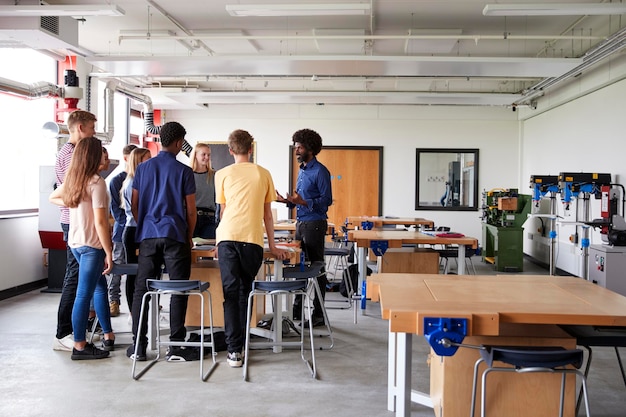 Grupo de estudiantes de secundaria de pie alrededor del banco de trabajo escuchando al maestro en la lección de diseño y tecnología