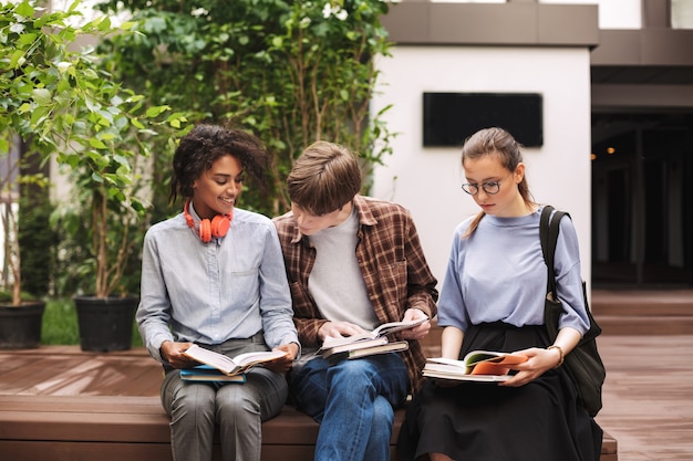 Foto grupo de estudiantes sentados en un banco y leyendo libros en el patio de la universidad