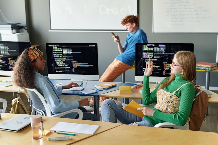 Foto grupo de estudiantes sentados en un escritorio con computadoras durante la lección de ti en el aula
