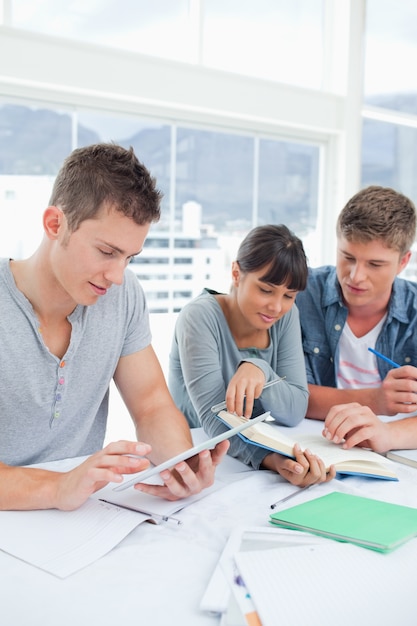 Un grupo de estudiantes se sientan juntos usando una tableta y un libro para estudiar